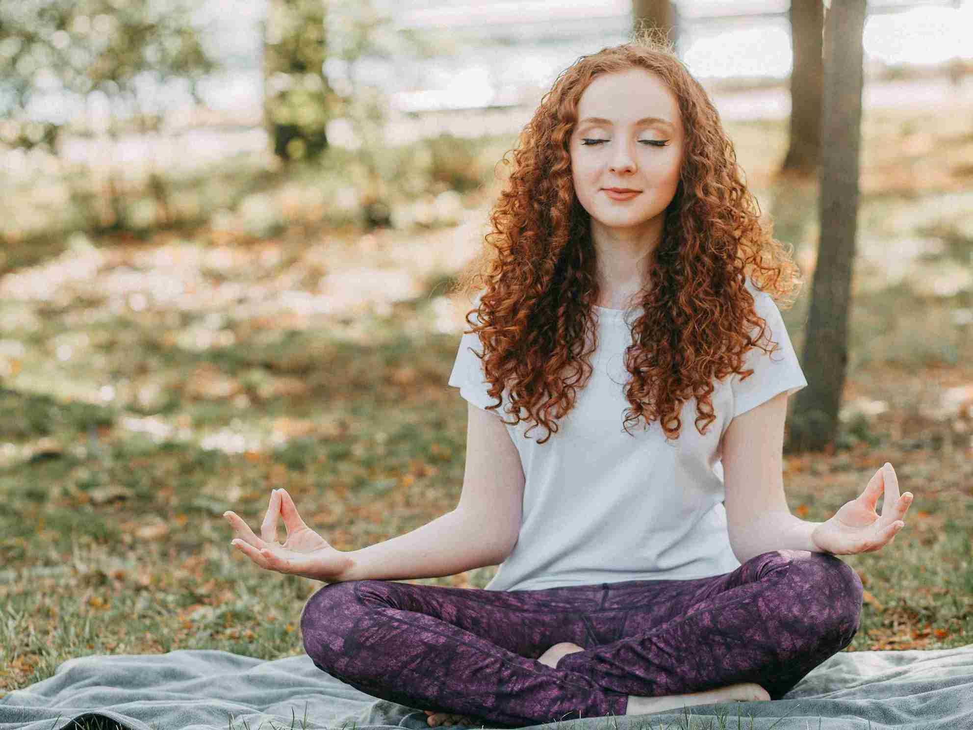 Woman practicing stress relief yoga in a peaceful outdoor setting, seated in a meditative pose with eyes closed, promoting relaxation and mental calm.